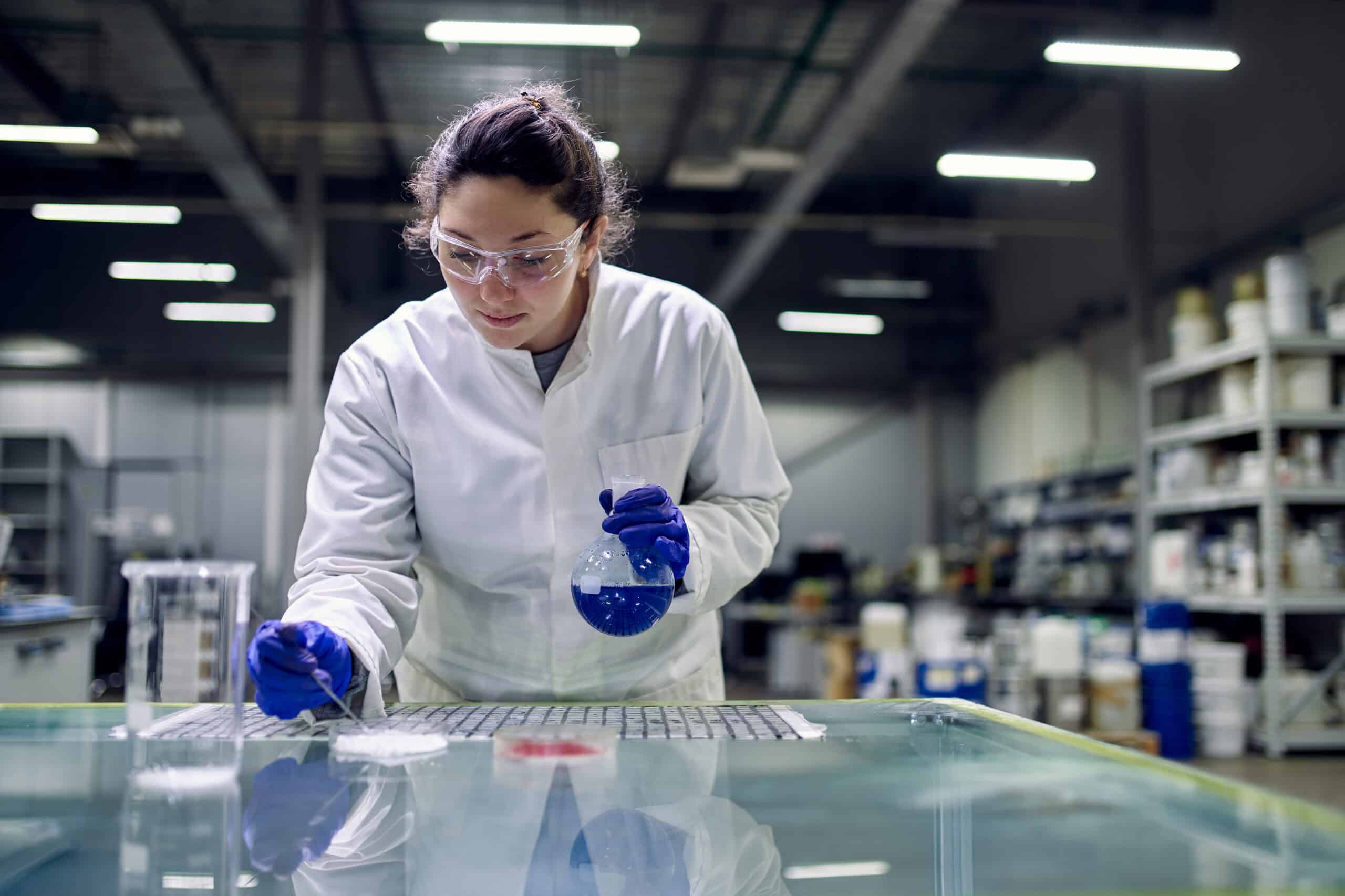 Laboratory brunette girl with flask with blue liquid in her hands checks quality